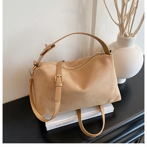 Detail of camel suede handbag featuring gold zipper and adjustable strap on a dark surface