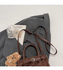 Close-up of brown suede crossbody bag with bow detail and plush bear charm