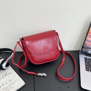 Detail of red faux leather saddle bag with silver peanut pendant on a dark desk