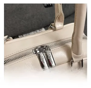 Detailed close-up of polished silver dual zippers on a beige textured leather tote bag
