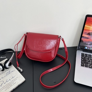 Detail of red glossy saddle bag with thin strap on a minimalist office desk setup