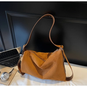Detail of caramel suede hobo bag with adjustable strap and metal hardware on a white desk