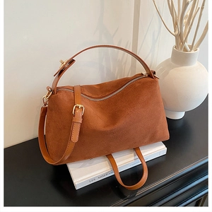 Detailed view of brown suede pillow bag on white books with elegant interior decor
