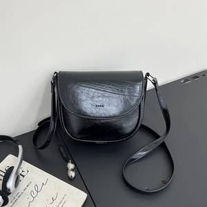 Detail of black semi-circular saddle bag in glossy leather with silver peanut charm