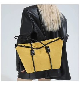 Detail of yellow suede tote bag with black woven strap and metallic rivet hardware