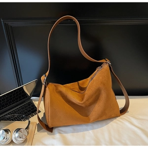 Detailed view of caramel suede tote bag next to a laptop and silver headphones
