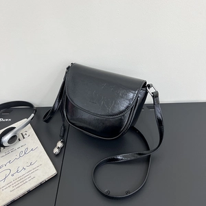 Close-up of black grainy leather saddle bag featuring a unique silver peanut-shaped charm
