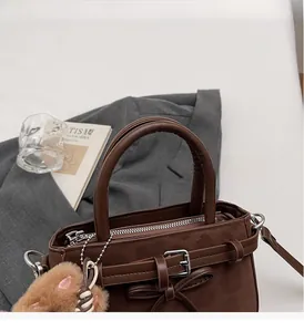 Detail of dark brown suede handbag with decorative bow and plush animal keychain charm
