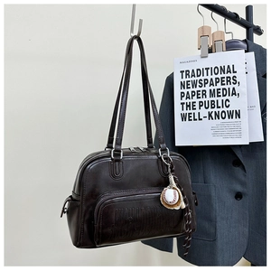 Detail of dark brown leather tote bag featuring front pocket and baseball charm