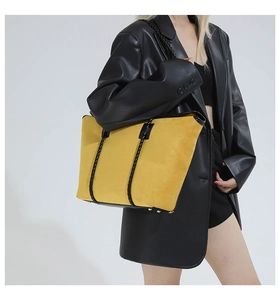 Detail showing bright yellow suede tote bag with black woven straps and metal feet