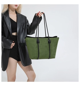 Detail of a large green suede tote bag with woven handles on a model in black leather jacket