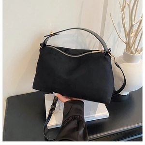 Close-up of matte black suede handbag with gold zipper and wide top handle