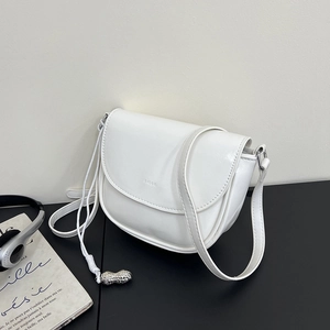 Detail of white saddle bag showing silver peanut-shaped charm and adjustable strap