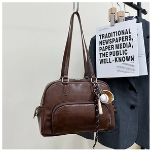 Detail of a brown leather tote bag with embossed letters and a baseball-themed charm