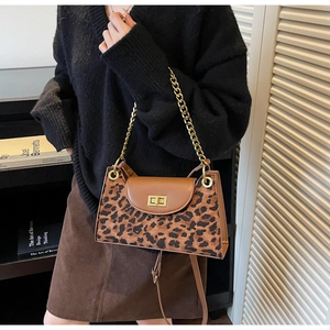 Detail of leopard print handbag with gold chain strap and turn-lock closure on model