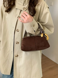 Deep brown suede Boston bag with gold chain accent shown on a model in a trench coat