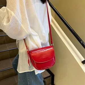 Detail of red saddle bag with glossy finish and unique silver peanut-shaped charm