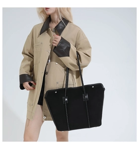 Detail of large black suede tote bag featuring intricate woven handles and metal rivets