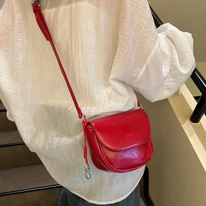 Detailed view of red saddle bag with unique silver peanut charm and glossy finish