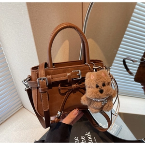 Detail of caramel crossbody bag with leather buckles, bow decor and plush dog charm