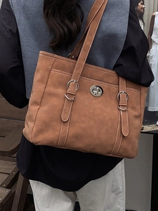 Large caramel leather tote bag with silver buckle worn on shoulder for autumn winter