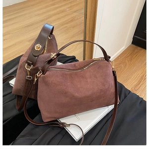 Close-up of brown suede pillow bag with leather handles and gold metal zipper detail