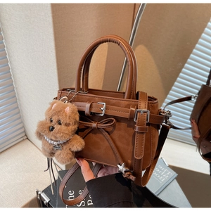Detail of vintage brown crossbody bag with bow accent and plush dog charm in soft light