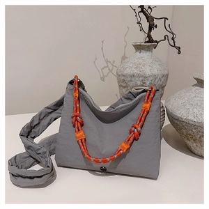 Detail view of a gray nylon dumpling bag with vibrant orange and blue braided rope accents