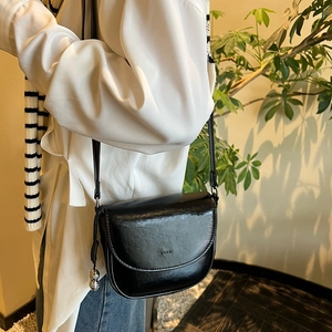 Detail of a black glossy leather saddle bag featuring a unique peanut-shaped metal charm