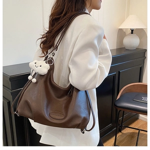 Close-up of brown leather hobo bag with embossed logo and white plush charm detail