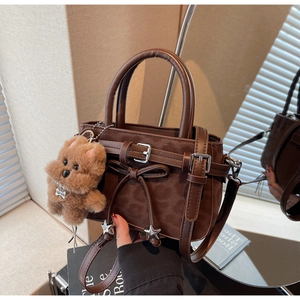 Detail of dark brown tote with leather bow, star charm, and plush bear keychain accessory