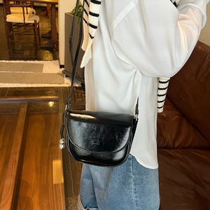 Detail of black pebbled leather saddle bag featuring a metal ball pendant and strap