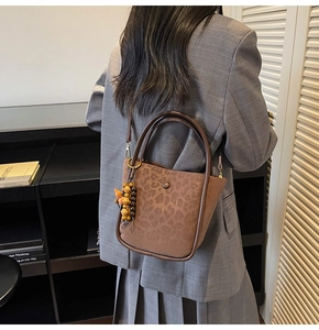 Detail of leopard print bucket bag with wooden bead charm worn with grey blazer