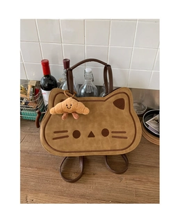 Detail of cute cat-shaped brown suede backpack with croissant plush charm on a table