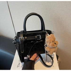 Detail of leopard embossed black mini bag featuring a decorative buckle and plush bear charm
