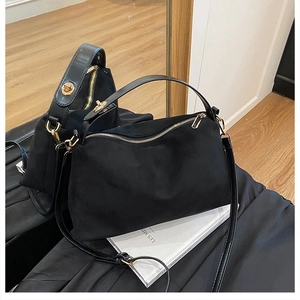 Detail of black suede doctor bag with shiny gold hardware and versatile shoulder strap