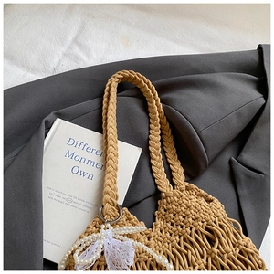 Detail of hand-woven mesh tote bag featuring a pearl chain and white lace bow accessory