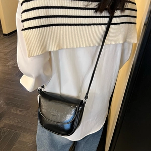 Detail of a minimalist black glossy saddle bag with thin strap worn by a model