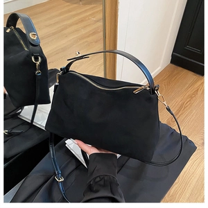 Detailed close-up of a black frosted suede handbag with gold zipper and leather handles
