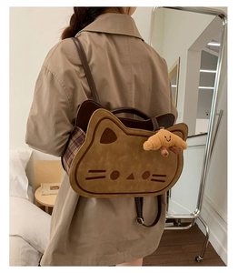 Detailed side view of khaki cat-shaped backpack with brown plaid accents and charm