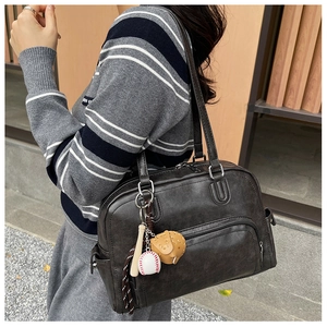 Close-up of black retro tote bag with textured synthetic leather and baseball charm