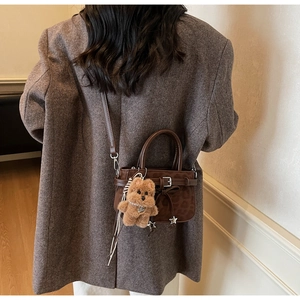 Detail of dark brown suede crossbody bag with vintage bow, star charm, and plush puppy