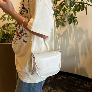 Side view of white saddle bag with woven knot and gold ball charms on a thin strap