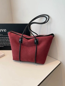 Large burgundy suede tote bag with black woven shoulder straps in a minimalist studio setting