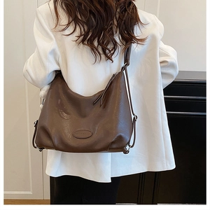 Detail view of large brown PU leather hobo bag with embossed logo on a white blazer
