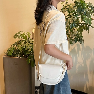 Model wearing a white saddle bag with a metallic ball charm in a stylish setting