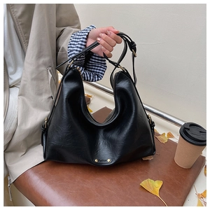 Detail der schwarzen Hobo-Tasche aus Kunstleder mit Goldplakette und Herbstlaub-Hintergrund