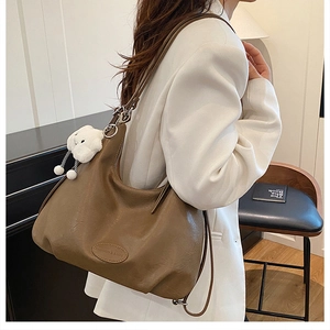 Detailed close-up of brown leather tote bag with fashion label and white cloud charm