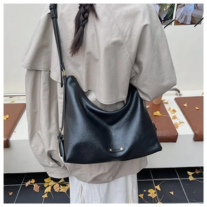 Detail der schwarzen Hobo-Tasche mit Goldplakette und breitem Riemen auf einem Herbstmantel