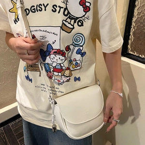 Side view of a minimalist cream saddle bag worn by a model against a textured wall